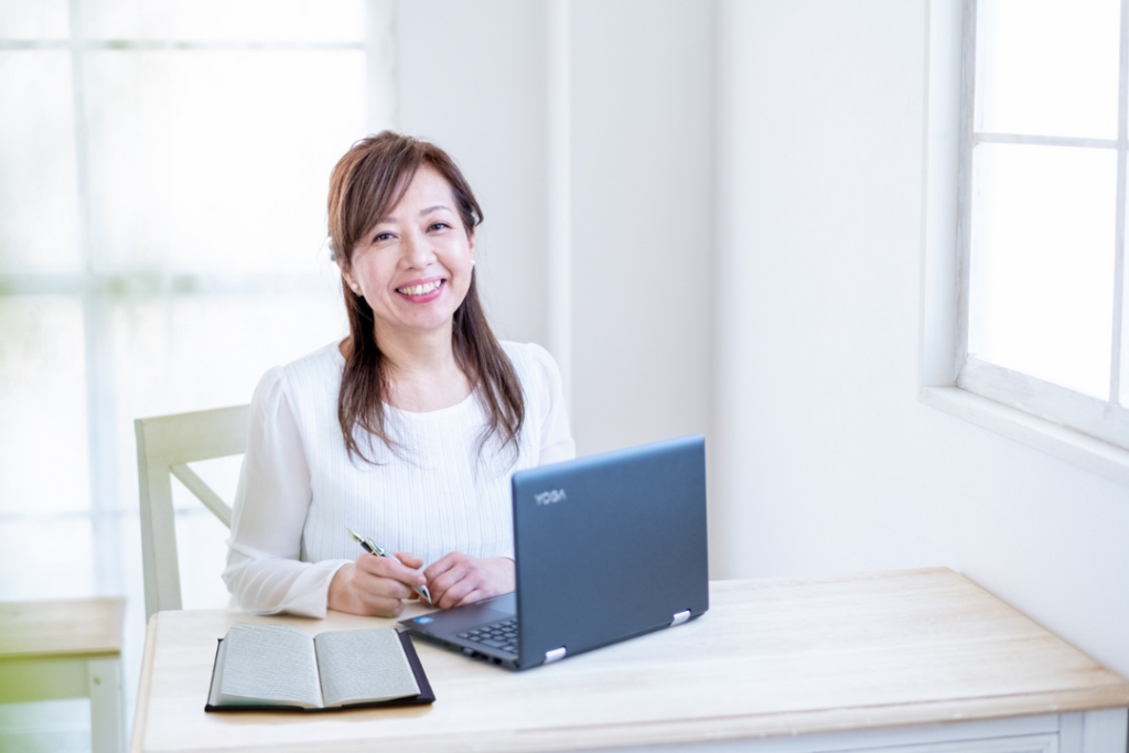 白色に統一された部屋で、女性がパソコンを前にこちらを向いてほほ笑んでいる